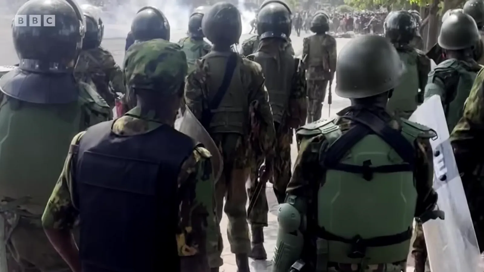 Kenyan riot police in body armour and helmets, seen from behind, advancing up Parliament Road.
